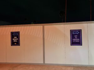 a construction wall with two signs on it. Pointing left: The Berlin Wall. Pointing Right: Exit to Universal Citywalk